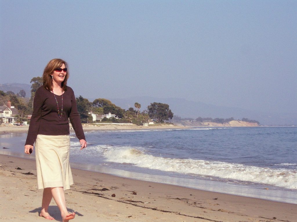 Renee strolling on a California beach, looking relaxed and glamorous, gazing to the horizon.